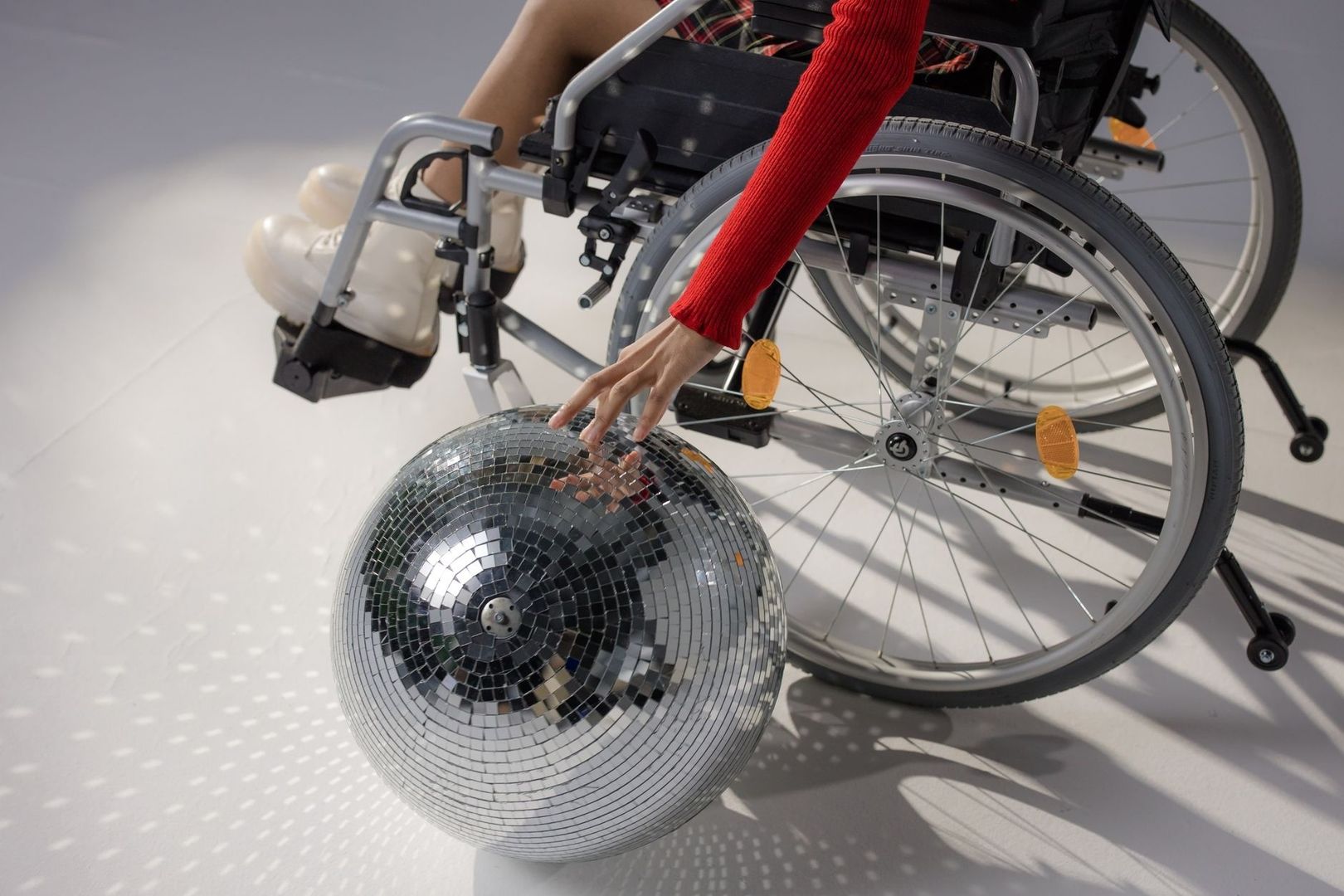 Wheelchair user reaching toward a disco ball on a bright floor