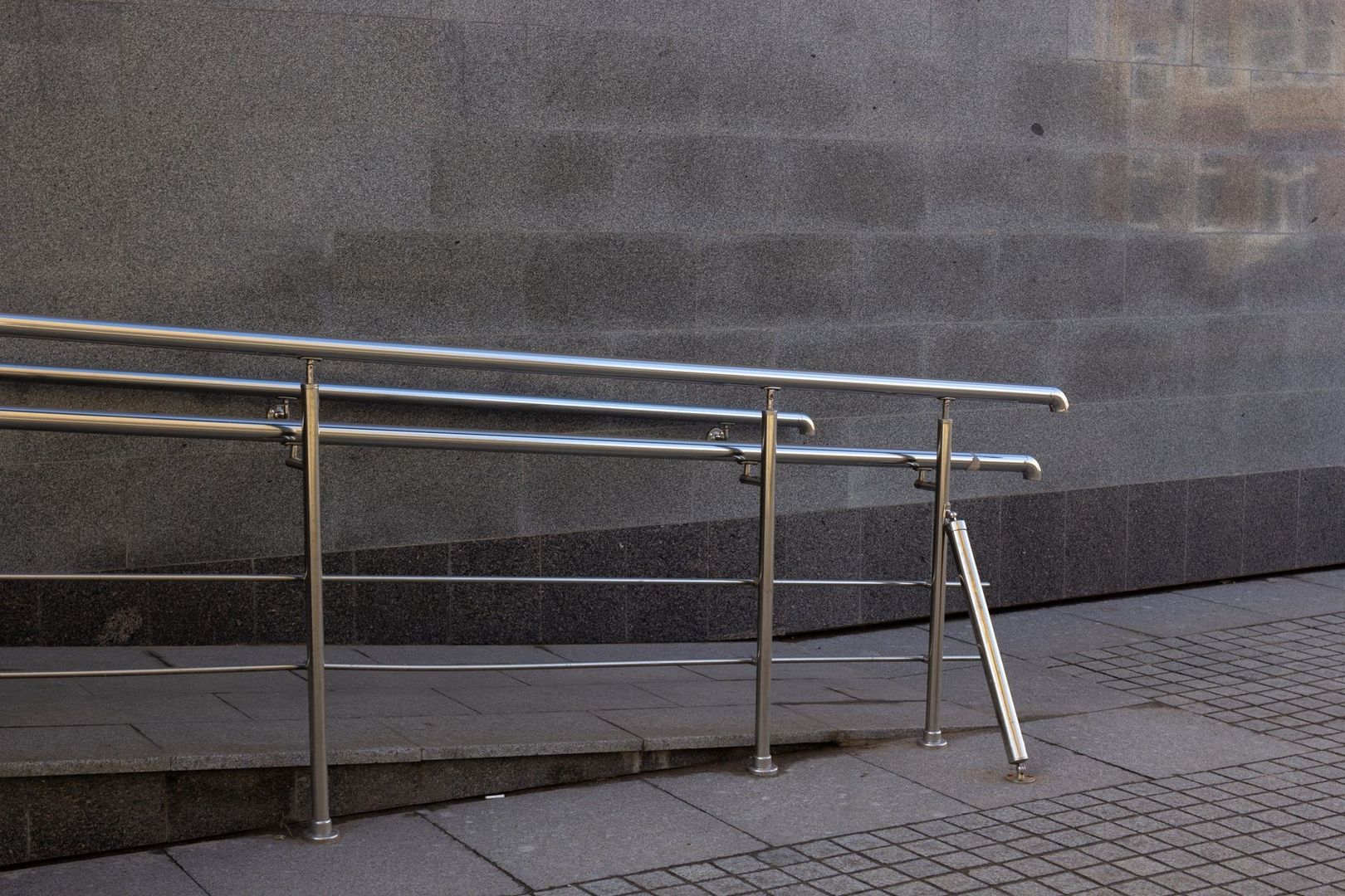 Stainless-steel handrails beside a ramp and steps outside a building